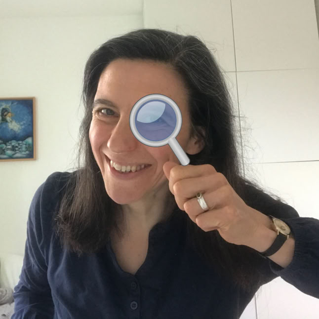 Frau schaut durch eine Lupe in die Kamera